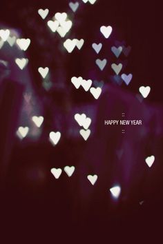 the words happy new year written in white hearts on a dark background with blurry lights