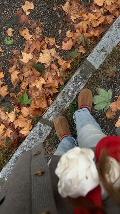 two people standing next to each other in front of leaves on the ground with their feet up