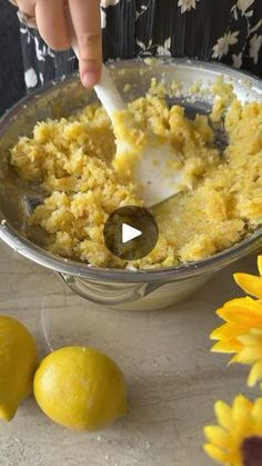 a person mixing food in a bowl with lemons and flowers around it on a table