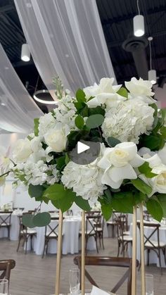 white flowers and greenery are arranged in gold vases on top of round tables