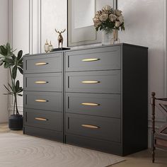 a black dresser with gold handles in a white room next to a mirror and potted plant