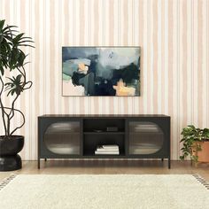 a living room with a painting on the wall next to a rug and potted plant