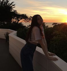 a woman standing on top of a balcony next to the ocean at sunset or sunrise