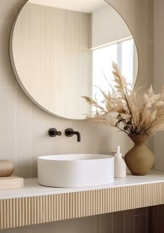 a bathroom with a round mirror above the sink and a vase filled with dry grass