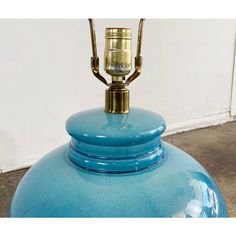 a large blue vase with a gold top and handle sitting on the floor next to a white wall