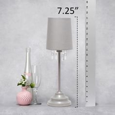 a table lamp next to a vase with flowers and a measuring tape on the wall