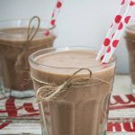 two glasses filled with hot chocolate drink on top of a wooden table next to straws