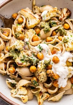 a bowl filled with pasta, broccoli and chickpeas covered in sour cream