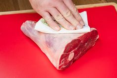 a person holding a piece of raw meat on top of a red cutting board next to a knife