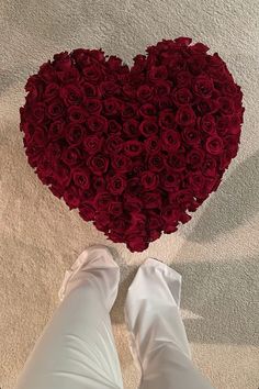 a heart shaped arrangement of red roses in someone's white pants and boots on the floor