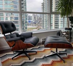 an eames chair and ottoman in front of a large window with cityscape