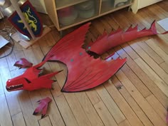 a red dragon laying on top of a wooden floor next to a book shelf filled with books