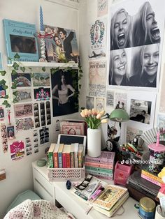 a white desk topped with lots of books and pictures next to a wall covered in photos