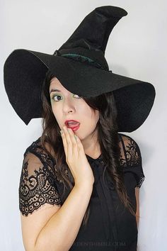 a woman wearing a black witches hat and holding her hand to her mouth while looking at the camera