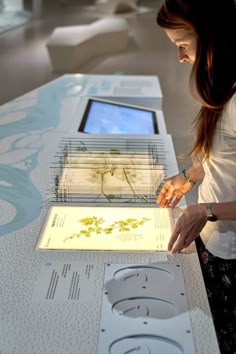 a woman standing over a table with an electronic device on it's display surface