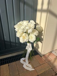 a bouquet of white roses sitting on the ground next to a door with a ribbon tied around it