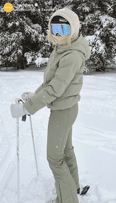 a woman standing in the snow with skis on her feet and wearing goggles