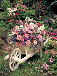 a wheelbarrow filled with lots of flowers in the grass next to some bushes