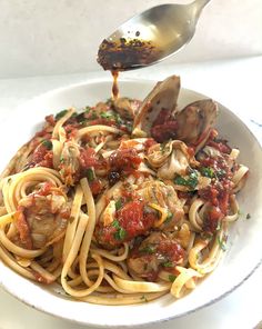 a plate of pasta with sauce and clams on the side is being drizzled with a spoon