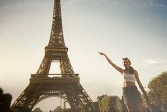 a woman standing in front of the eiffel tower with her arms raised up