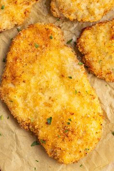 four pieces of fried chicken sitting on top of parchment paper with parmesan cheese