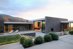 a modern house in the middle of a grassy area with mountains in the back ground