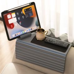 a table with a coffee cup and remote control sitting on top of it next to a tablet