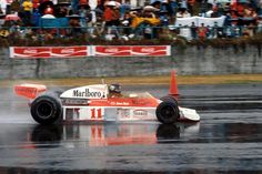 a man driving a race car on top of a wet track in front of a crowd