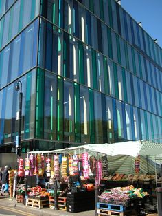 an outdoor market in front of a large building with lots of glass on the side