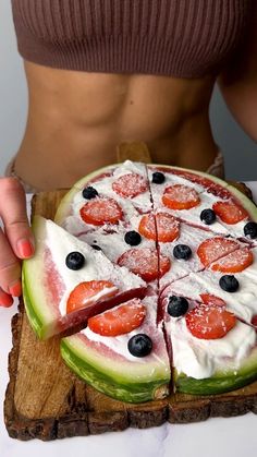 a woman is cutting into a watermelon and blueberry pizza