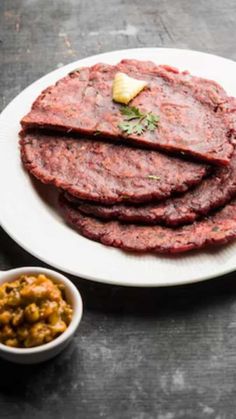 a white plate topped with meat patties next to a bowl of mustard and seasoning