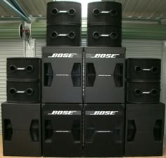 several black speakers stacked on top of each other in front of a metal garage door