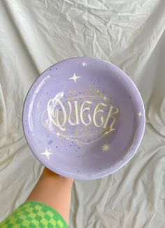 a hand holding a purple bowl with the word queen written in white letters on it