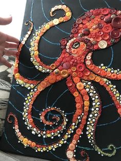 an octopus made out of buttons on a piece of black paper with white and orange thread