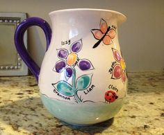 a ceramic pitcher with flowers and ladybugs painted on the side sitting on a kitchen counter