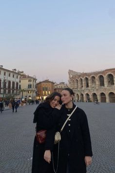 two people standing in front of an old building and looking at the camera with their arms around each other