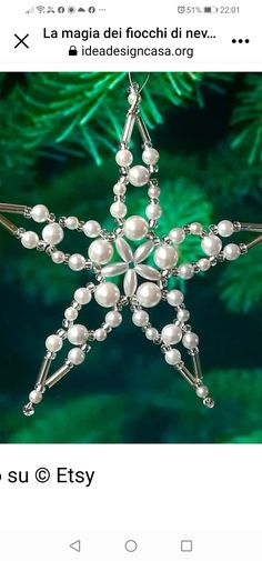 a christmas ornament with pearls and beads on the bottom, in front of a pine tree