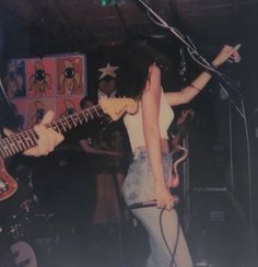 a woman holding a guitar while standing in front of a microphone and other musical instruments