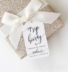 a gift wrapped in gold glitter with a white ribbon and thank you tag on it