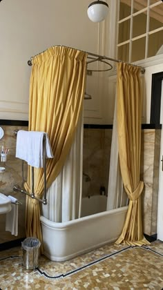 a bath tub sitting next to a window covered in yellow curtained drapes on top of a tiled floor