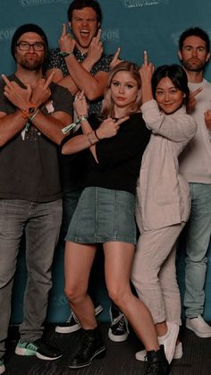 a group of people standing next to each other in front of a blue wall holding their hands up