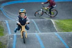 a young boy riding a wooden bike down a hill with another child on the other side