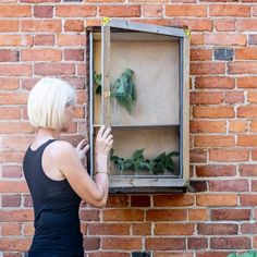 a woman standing in front of a brick wall looking at a display case filled with plants