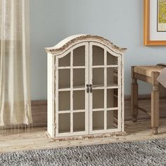 a white cabinet sitting on top of a wooden floor next to a chair and table