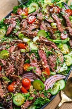 steak salad with tomatoes, cucumbers and onions in a black bowl on a wooden table