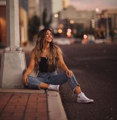 a woman sitting on the side of a road next to a street sign with buildings in the background