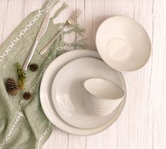 two white dishes with pine cones and silverware