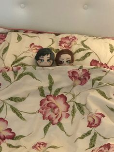 two dolls sitting on top of a bed under a white comforter with pink flowers