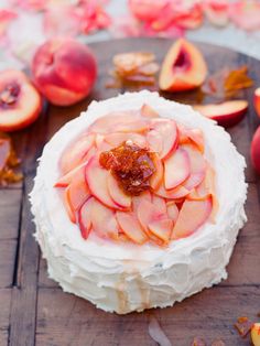 a cake with sliced peaches on it sitting on top of a wooden table next to slices of fruit