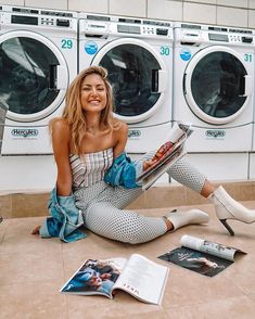 a woman sitting on the ground in front of washers with her legs crossed and holding a magazine